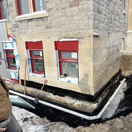 Drain français et membrane d'imperméabilisation noire installés le long d'une fondation en pierre lors de travaux hivernaux