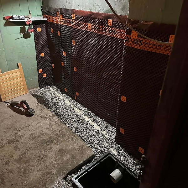 Membrane de drainage alvéolée et lit de gravier installés contre un mur de sous-sol pour système de drain français