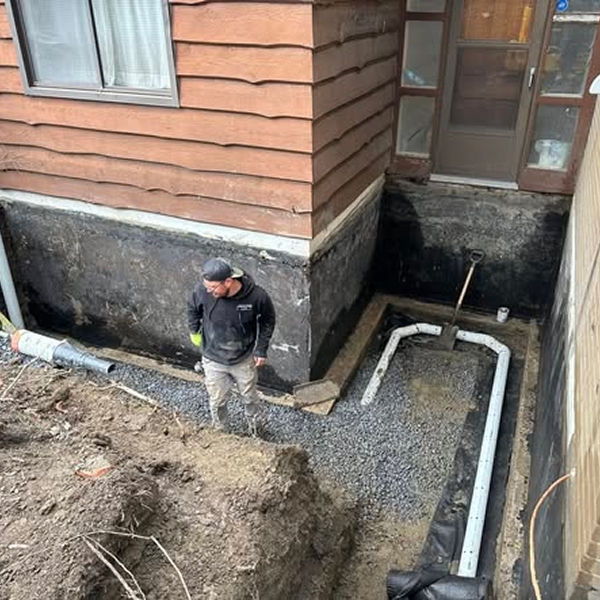 Technicien supervisant l'installation d'un drain français en gravier le long de la fondation extérieure d'une maison